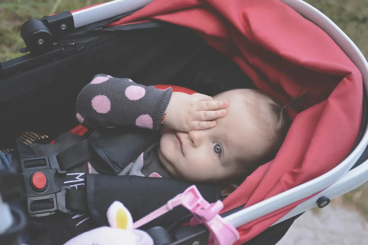 baby lying on stroller while covering eye during daytime