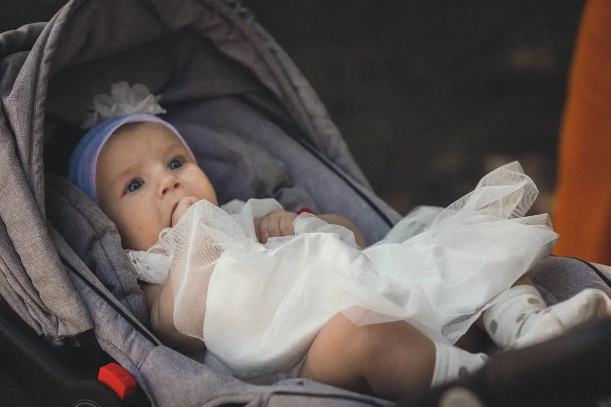 a baby in a stroller wearing a white dress