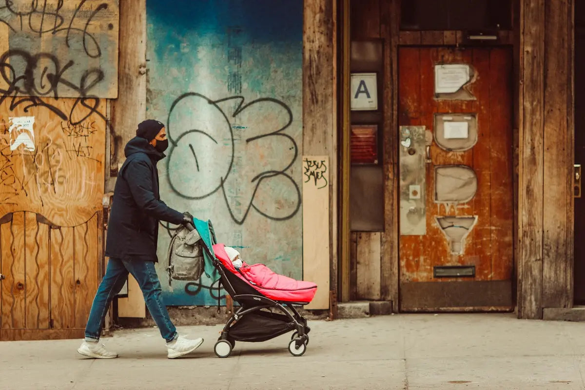 man in black jacket and blue denim jeans walking with black and red stroller