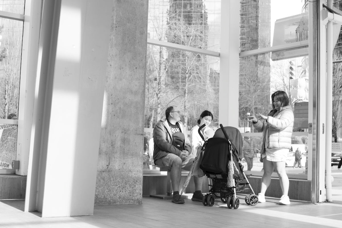A family with a baby in a stroller in a sunlit glass-walled transit station